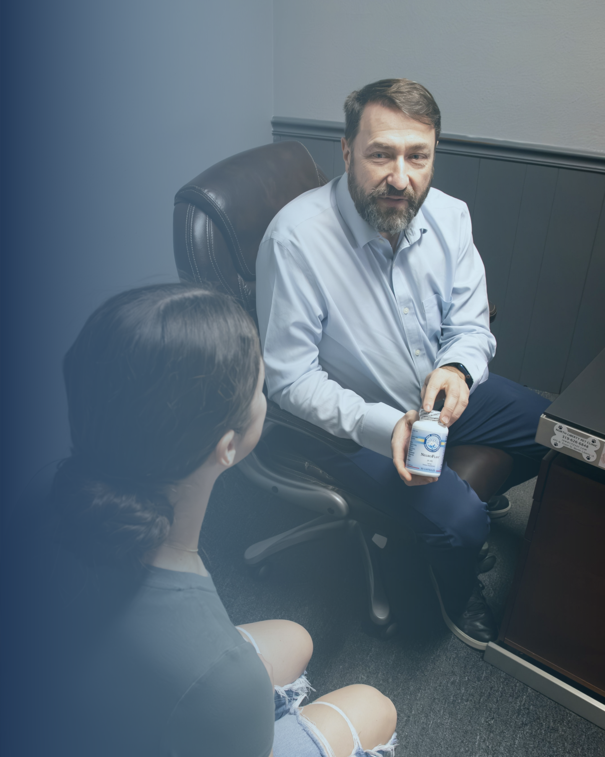 A male doctor presents a bottle of vitamins to a young women while sitting across from one another.